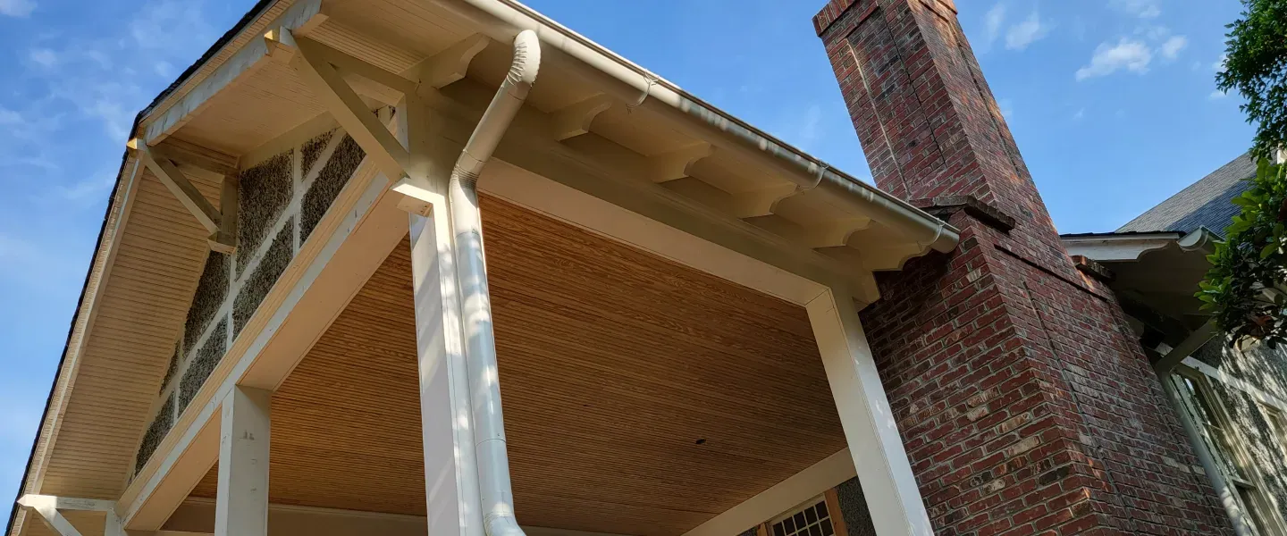 Brick chimney, wooden porch ceiling, white pillars, and blue sky.