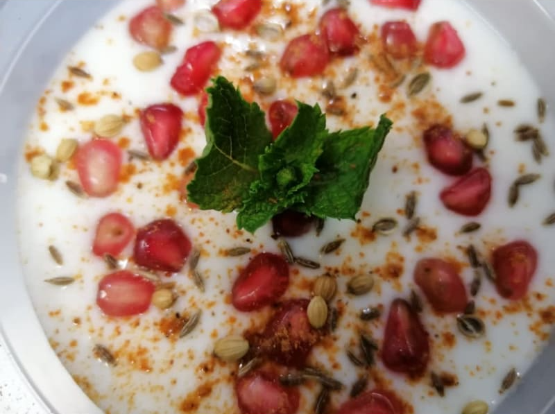 A bowl of yogurt with pomegranate seeds and mint leaves on top.