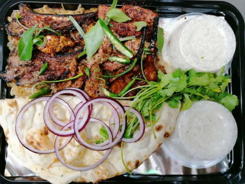A tray of food with meat , bread , onions and sauces.