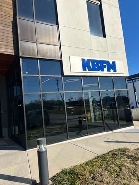 Exterior view of KBFM radio station building with blue signage and reflective windows.