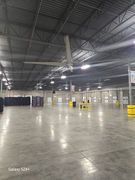 Large, empty warehouse with tall ceilings, concrete floor, and large overhead fan.