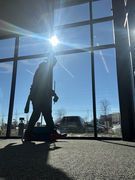 Silhouette of a person walking past a large window with bright sunlight and a clear blue sky.