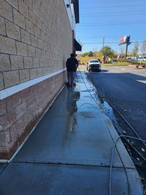 A person power washing a concrete sidewalk next to a brick building.