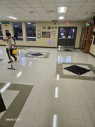 Person mopping a shiny tile floor in a well-lit hallway with glass doors and windows.
