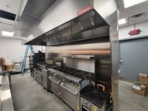 Commercial kitchen with stainless steel appliances and ventilation hood.