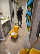 Man mopping floor in a brightly lit store aisle; yellow bucket, shelves of products on the right, sliding barn door in the background.