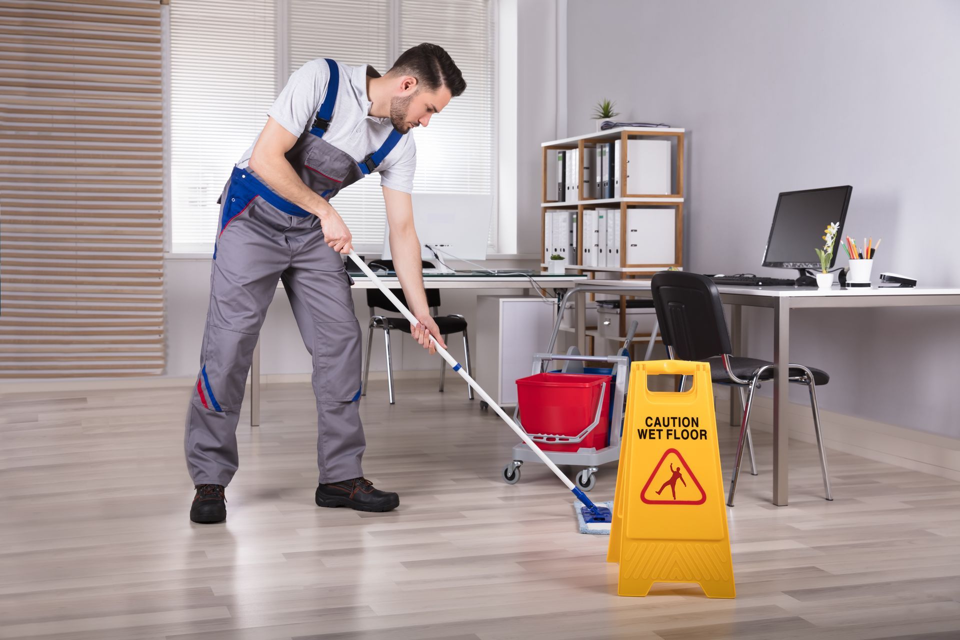 Janitor mopping office floor next to a caution wet floor sign. Janitor mopping office floor next to a caution wet floor sign.