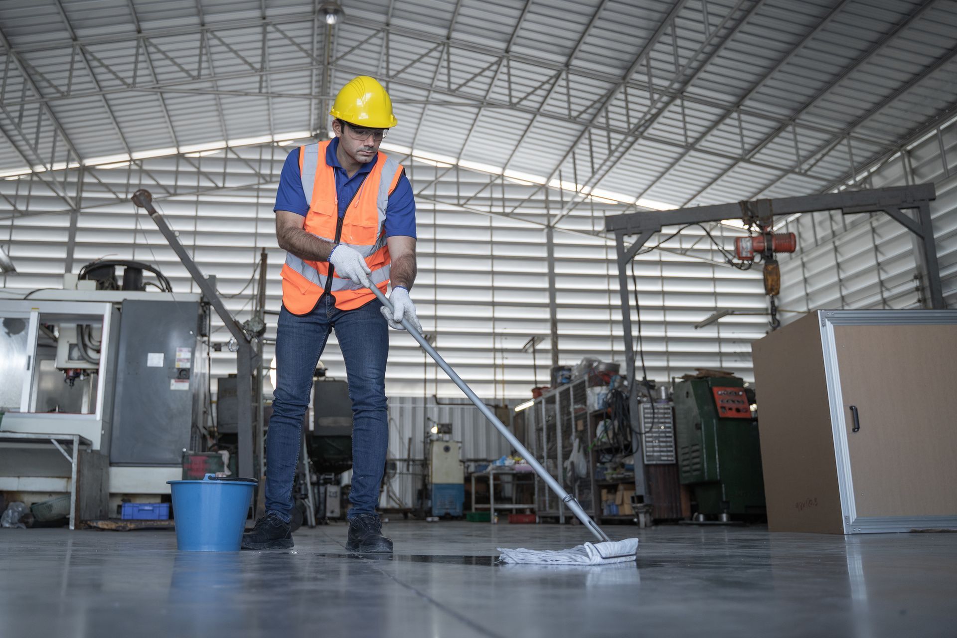 Worker mopping industrial floor with safety gear in large facility.