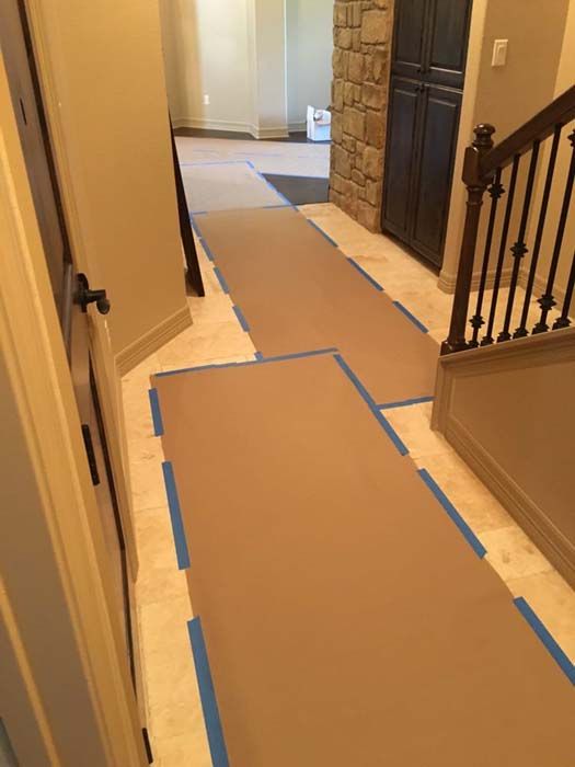 Brown paper taped to tile floor in a home hallway, protecting the surface. A staircase is visible.
