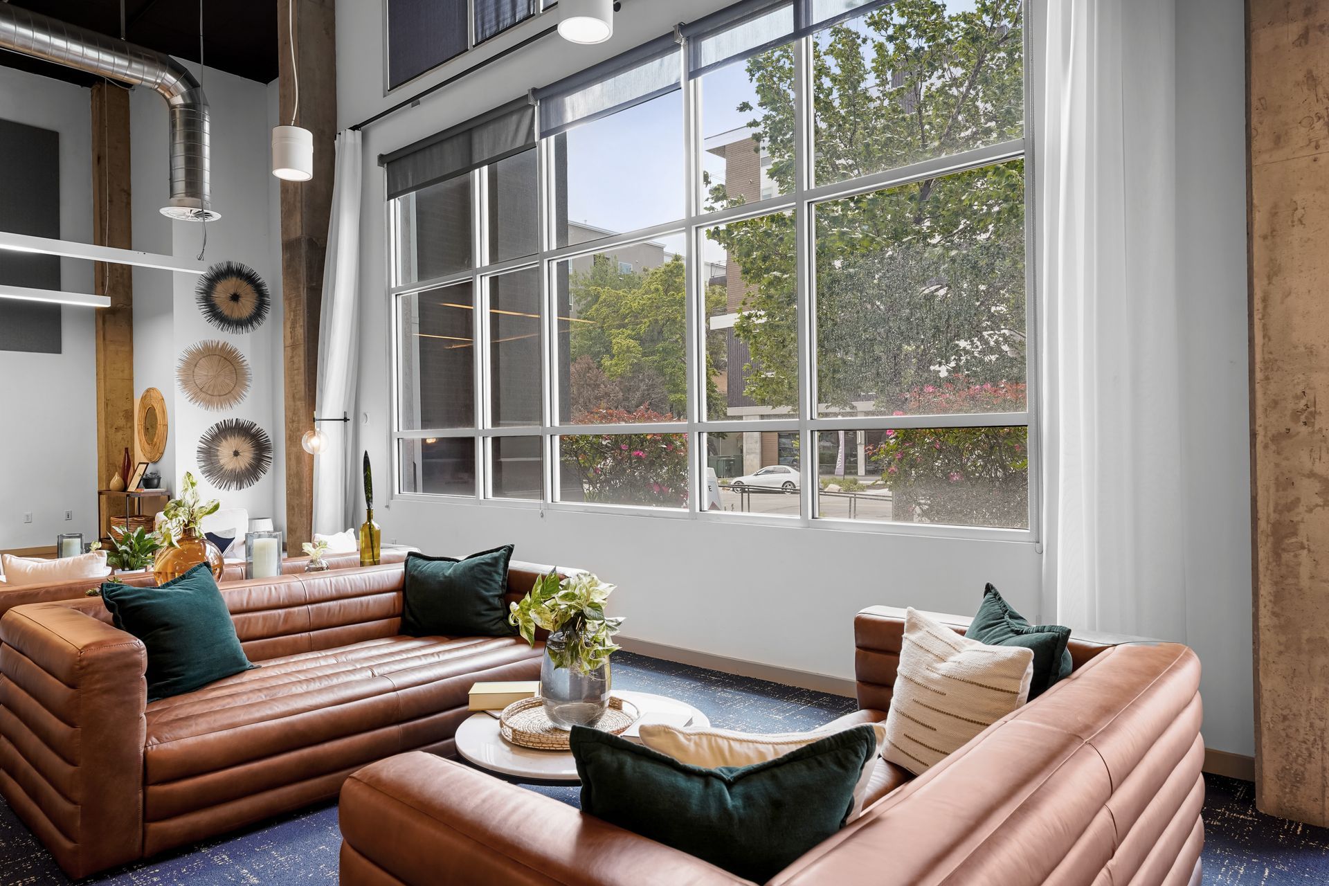 Modern lounge area with brown leather couches, large windows, and decorative wall hangings.