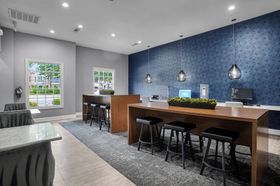 Modern lounge with communal tables, stools, computers, and decorative blue wallpaper.