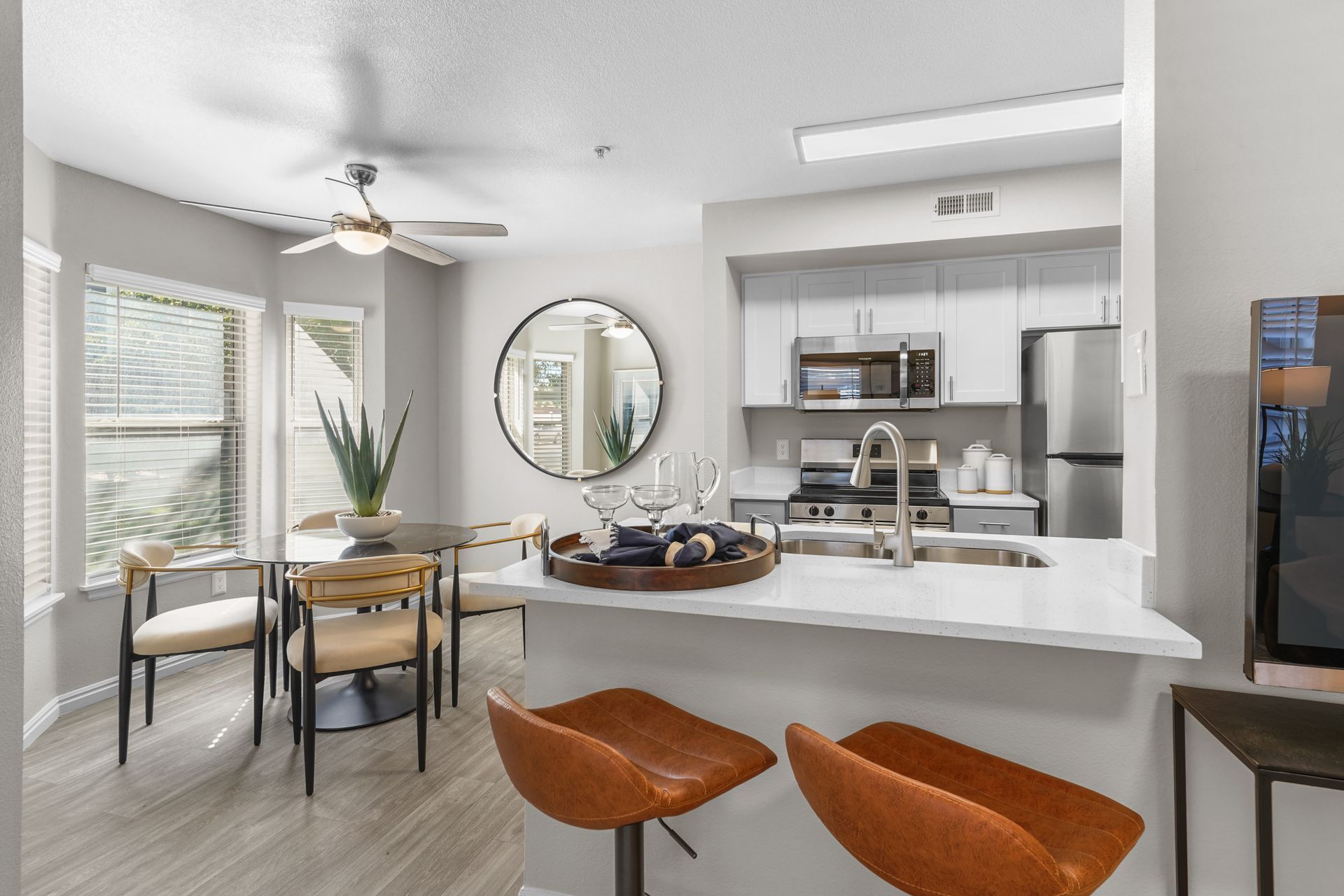 Interior view: kitchen with white cabinets, stainless steel appliances, breakfast bar with stools, dining table.