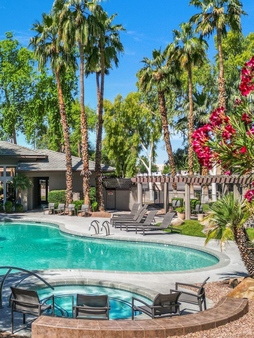 Pool area with turquoise water, lounge chairs, palm trees, and red flowers under a blue sky.