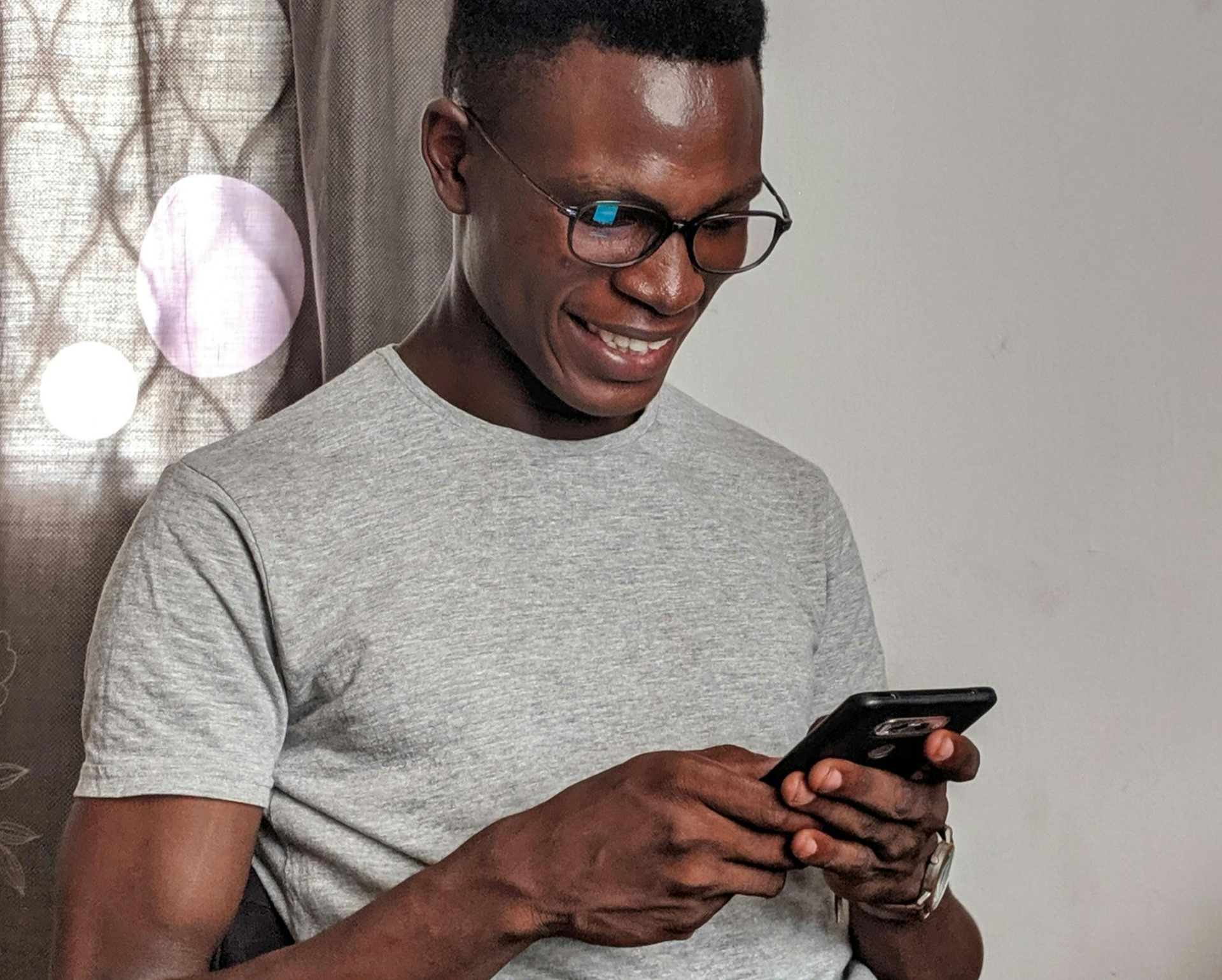 Smiling man with glasses using a smartphone, inside.