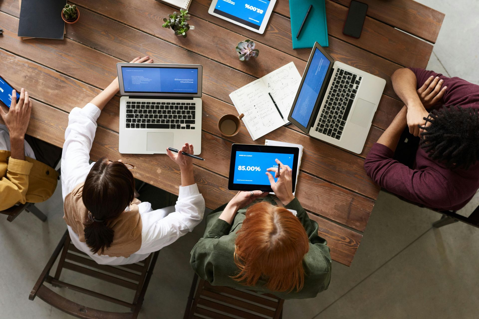 People around a wooden table with laptops and tablets, working together.
