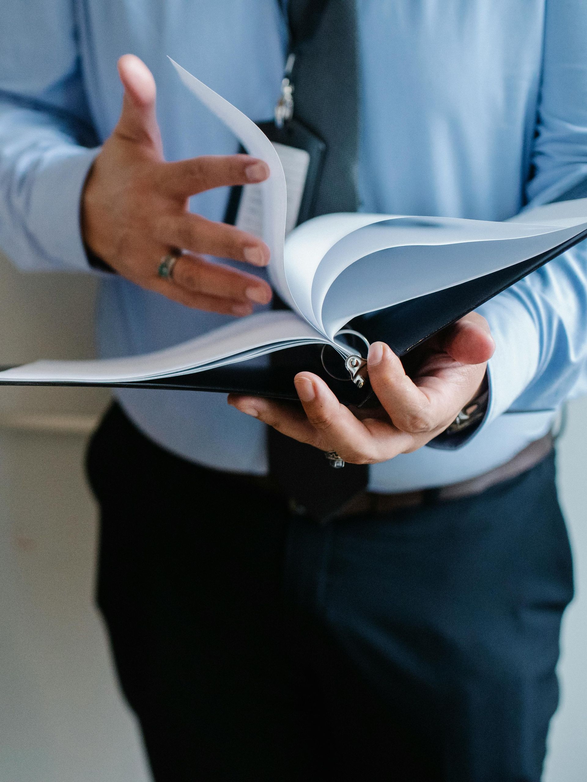Person in a blue shirt and black pants holding a binder, flipping through the pages.