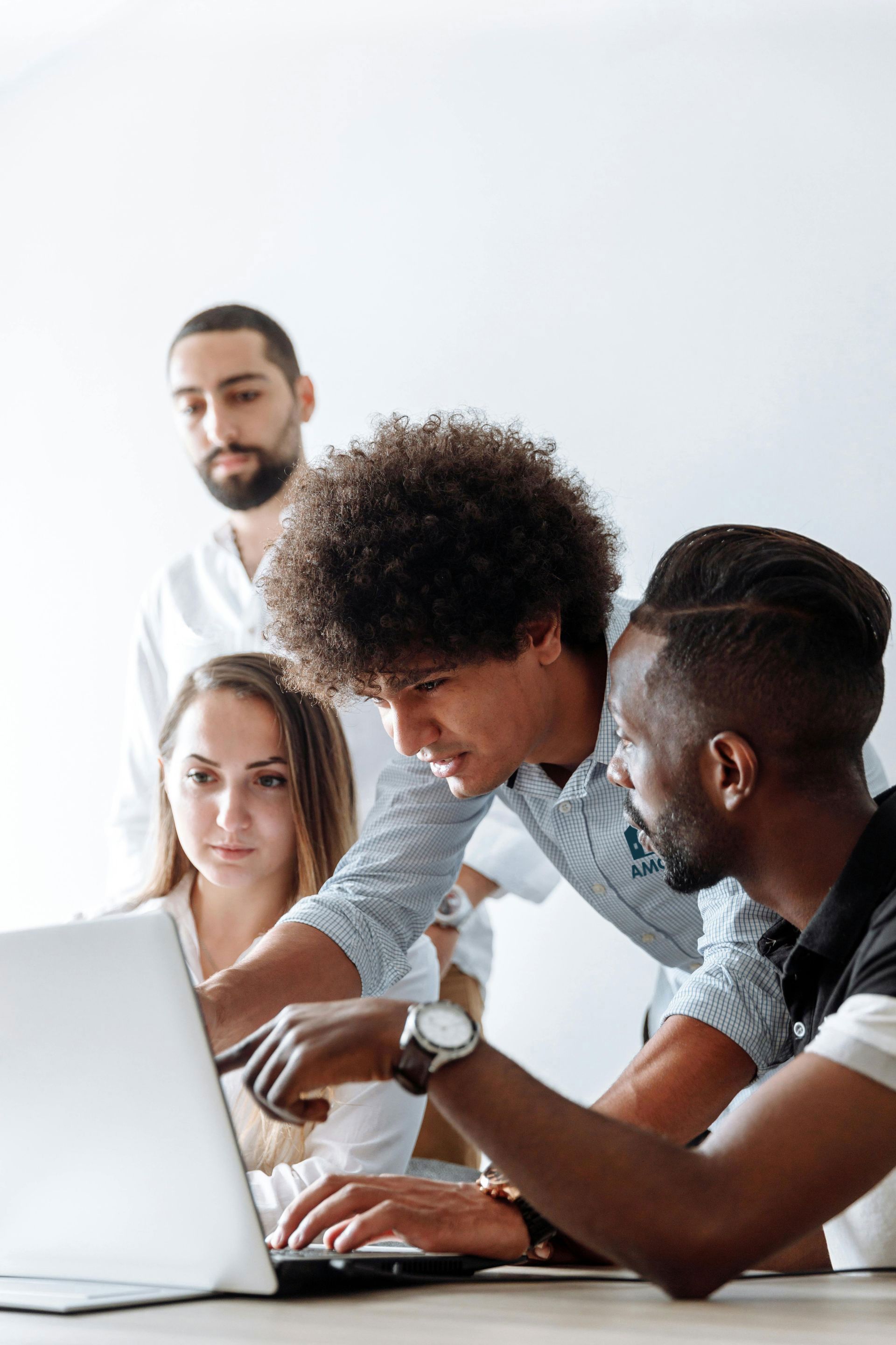 Group of diverse colleagues collaborating around a laptop, focused on the screen. Two men point; others look on intently.