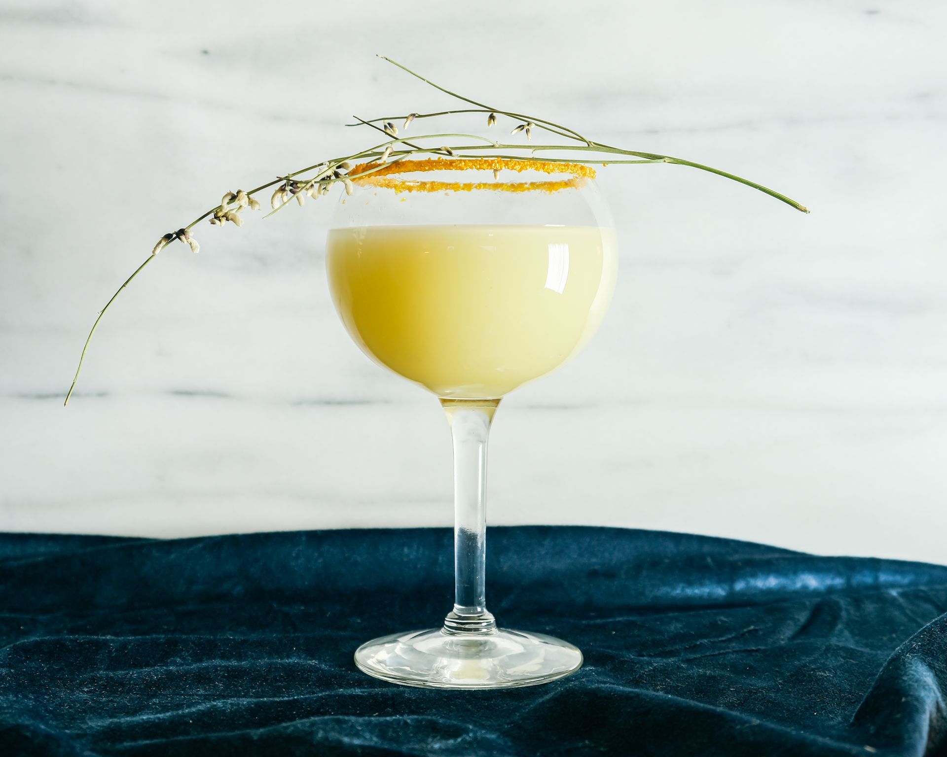 A yellow drink in a wine glass with a sprig of lavender on top.