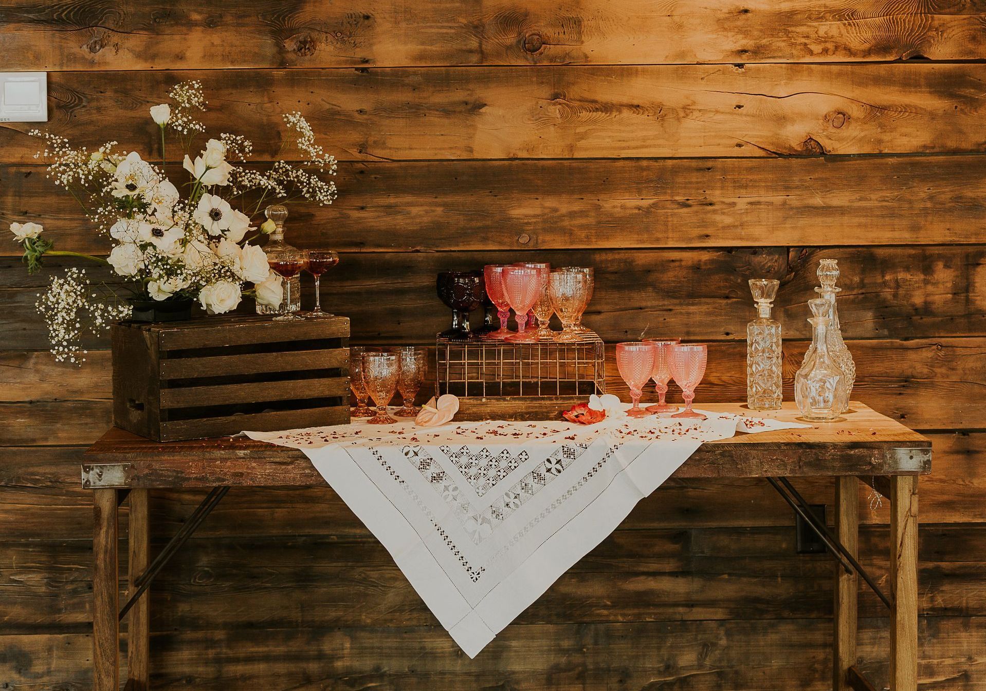 A wooden table with glasses and bottles on it in front of a wooden wall.