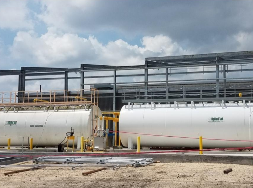Two large white tanks are sitting in front of a building under construction.
