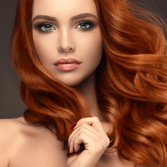 A woman with long red hair and blue eyes is holding her hair.