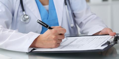 A doctor is writing on a clipboard with a pen.
