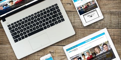 A laptop , tablet , and cell phone are sitting on a wooden table.