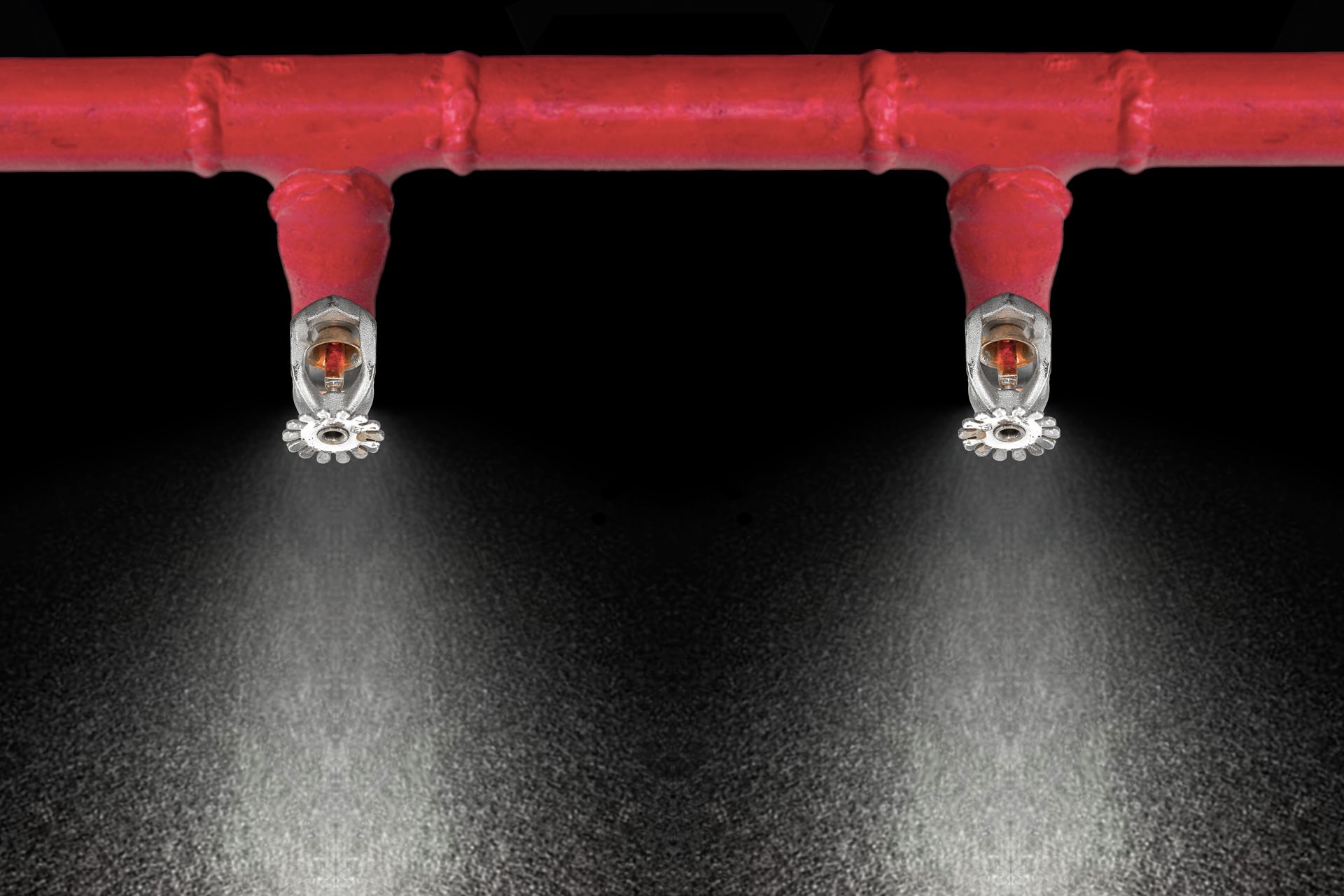 Active fire sprinkler heads spraying water from a red overhead pipe during operation.