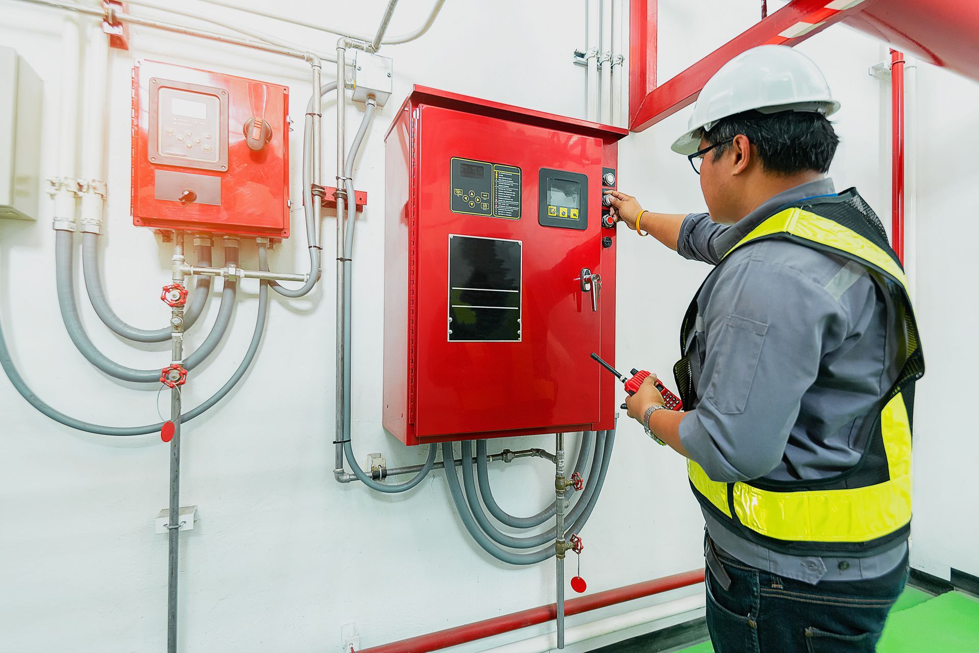 Worker in safety vest inspecting red fire control panel and wiring system indoors.