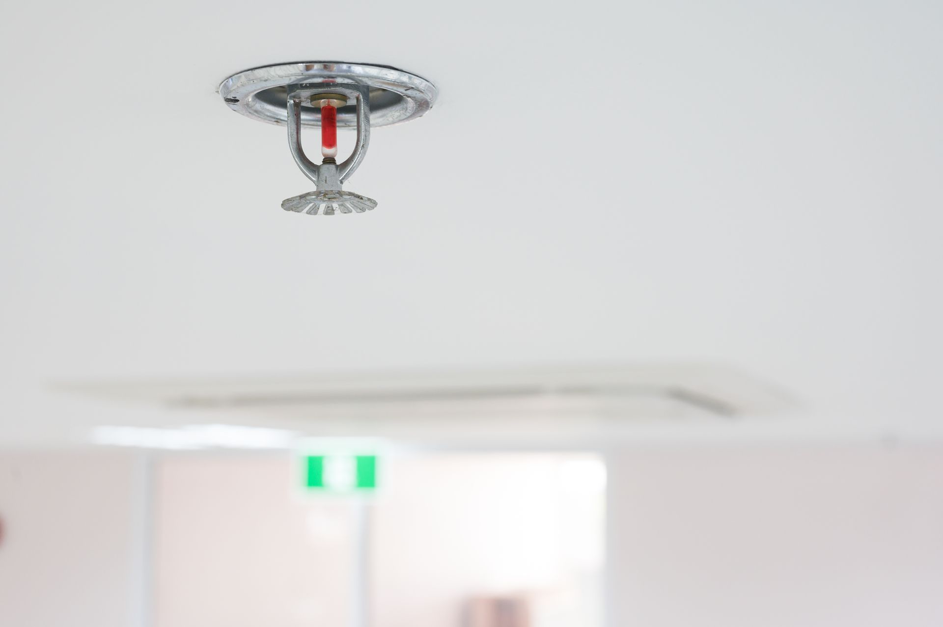 A close-up of a fire sprinkler installed on a white ceiling inside a room.