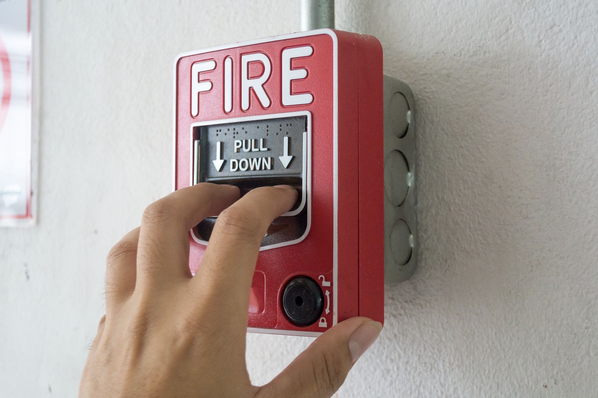The hand of man is pulling fire alarm on the wall next to the door 
