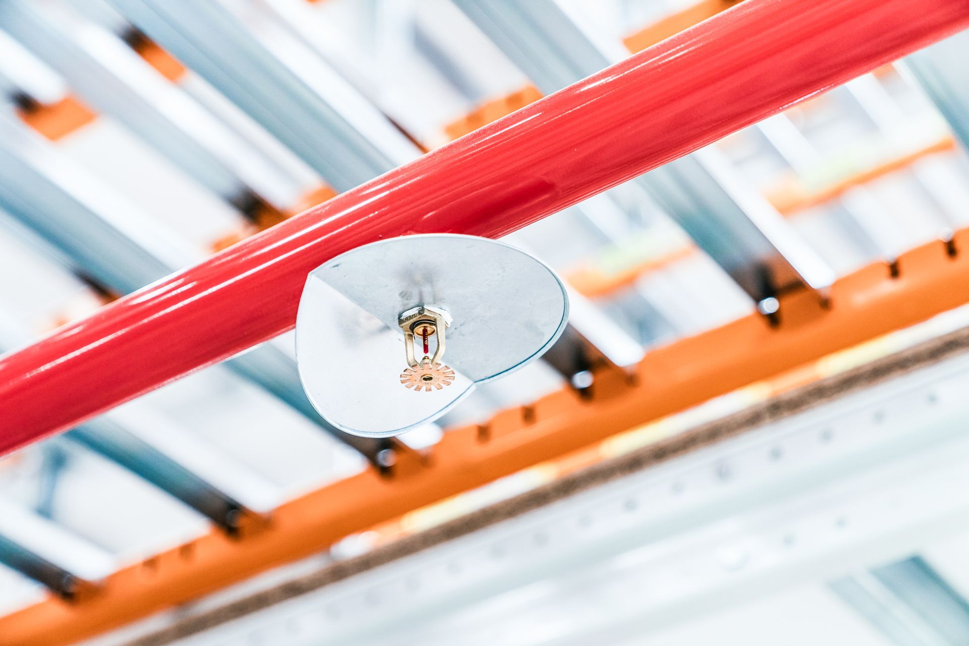 Close-up of ceiling-mounted fire sprinkler system with red pipeline in warehouse.