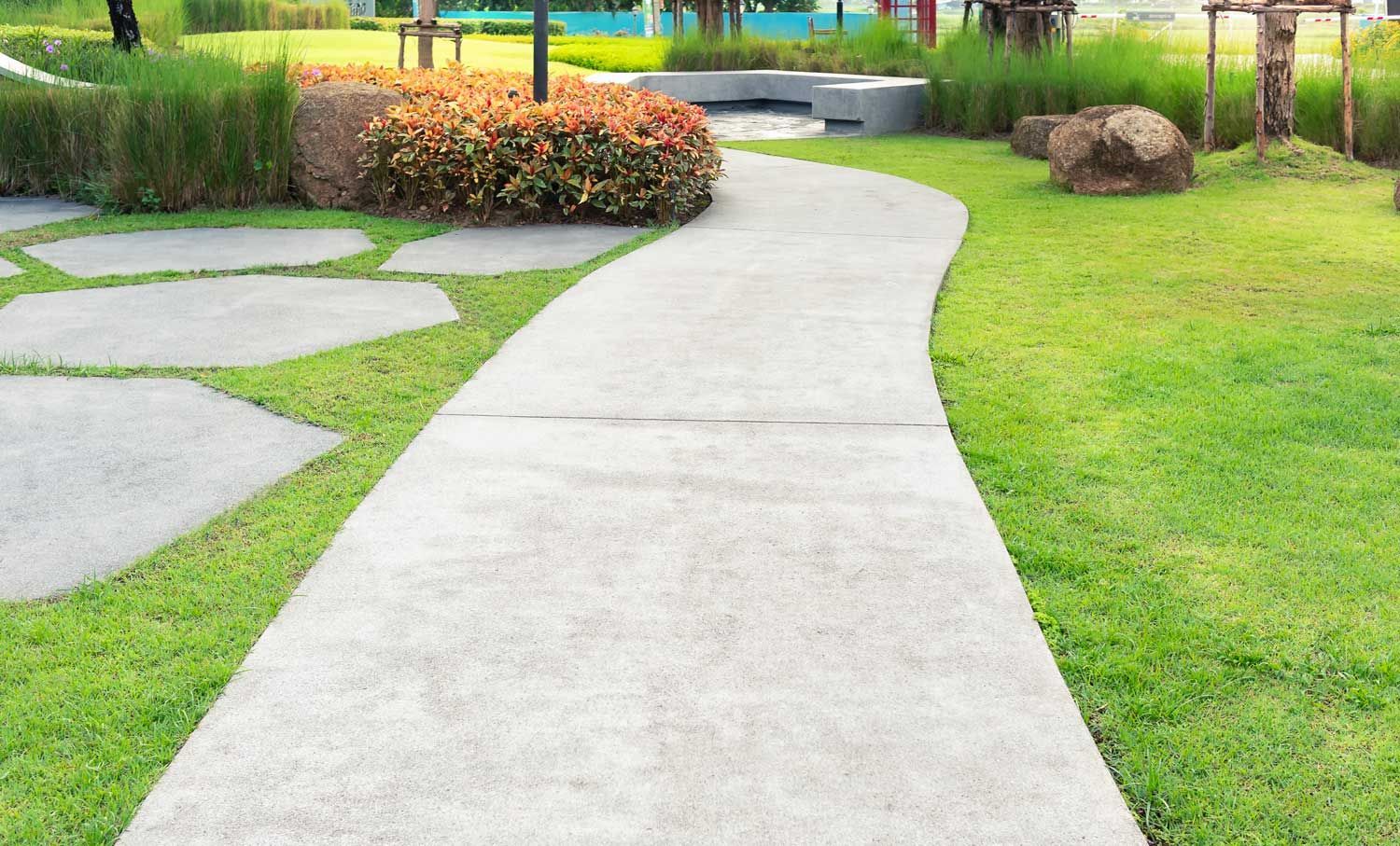 Concrete pathway winding through a grassy garden, with stepping stones and green foliage on either side.