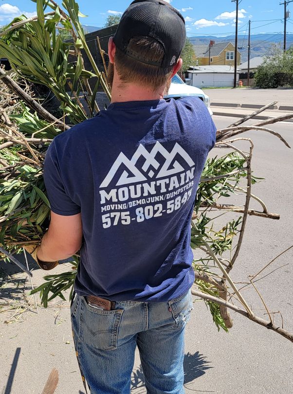 a man in a blue shirt is carrying a pile of branches .