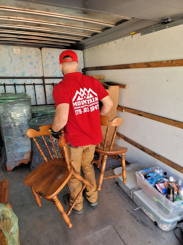 a man in a red shirt is holding two wooden chairs in a truck .