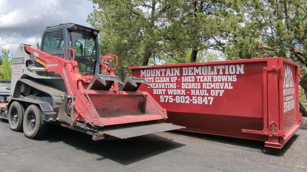 a red 20 yard dumpster is sitting next to a skid steer on a trailer.