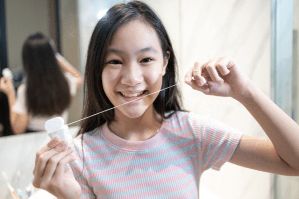 A young girl is flossing her teeth in front of a mirror.