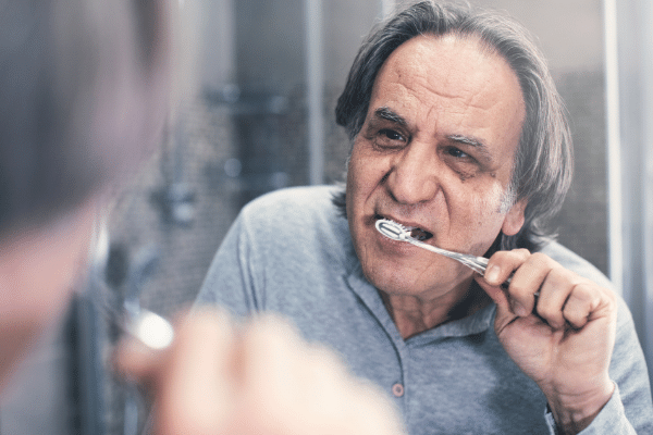 An older man is brushing his teeth in front of a mirror.