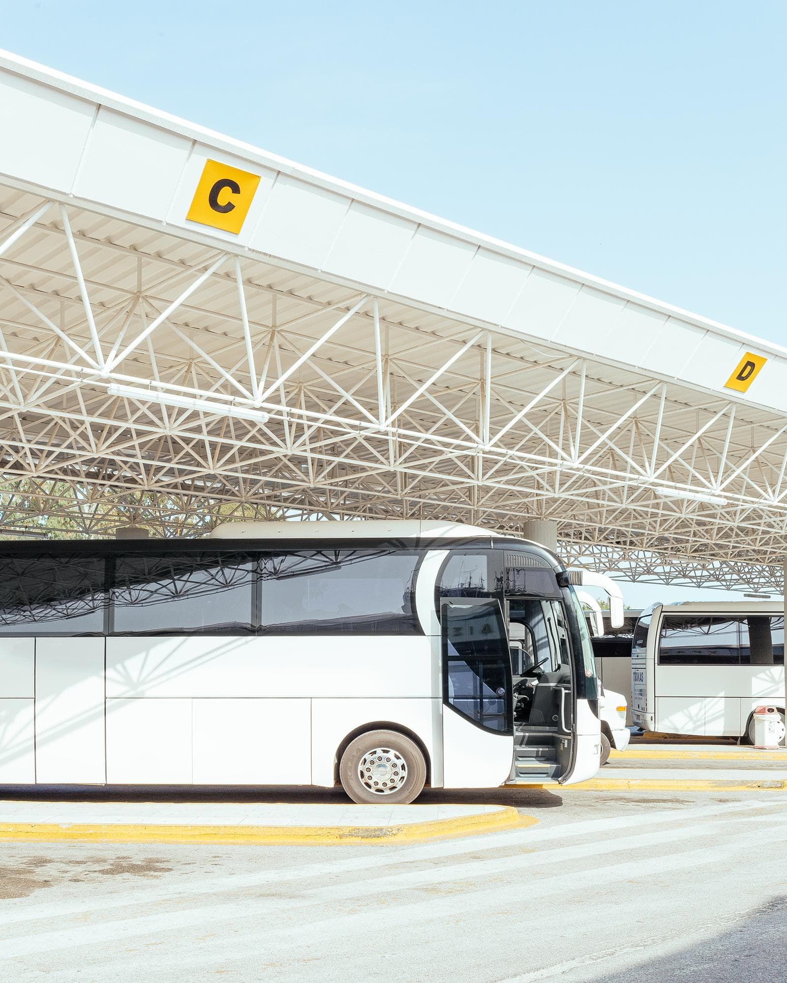 Ônibus branco estacionado em uma rodoviária, sob um toldo branco com as letras