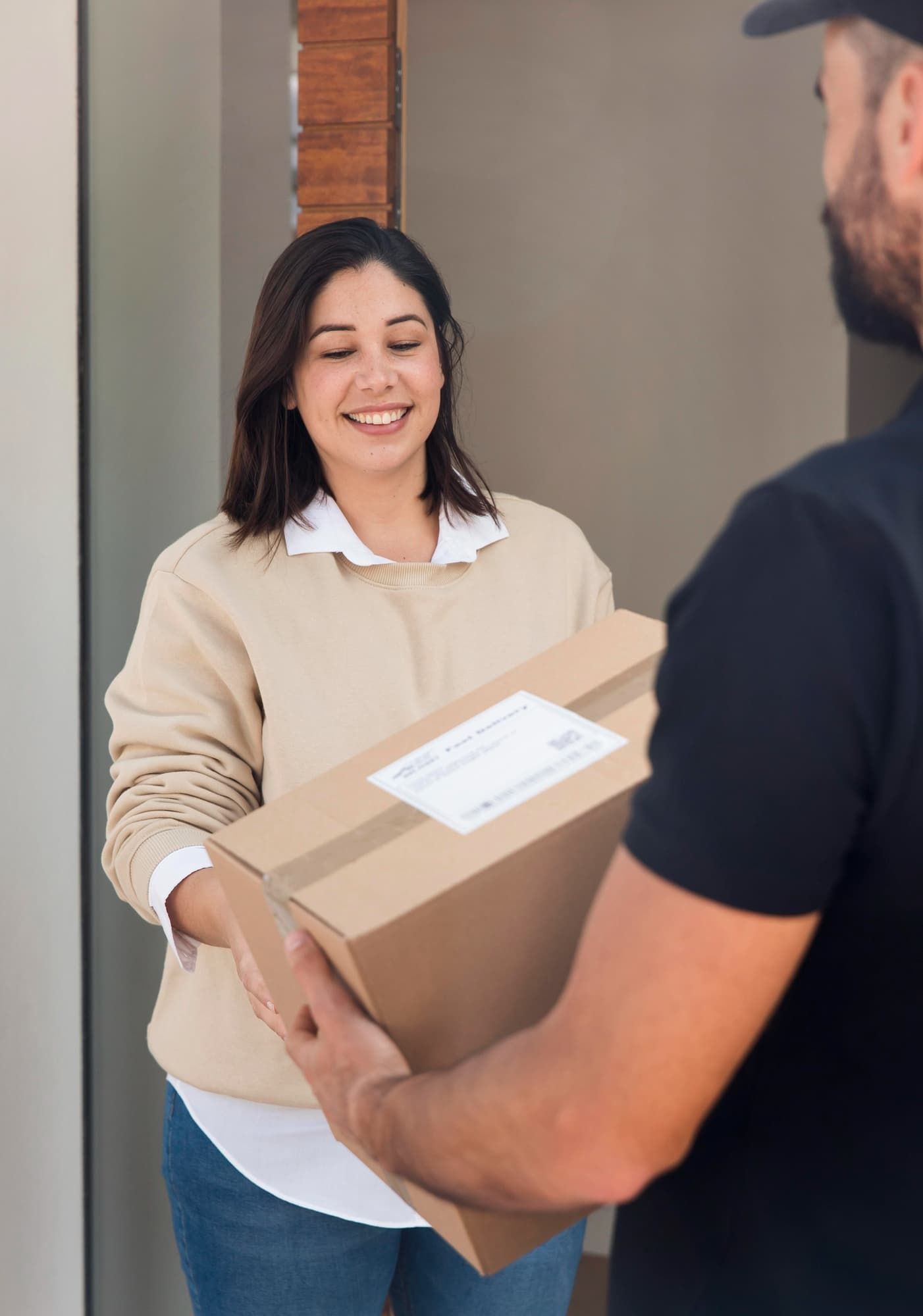 Mulher sorrindo ao receber um pacote de papelão do entregador na porta.