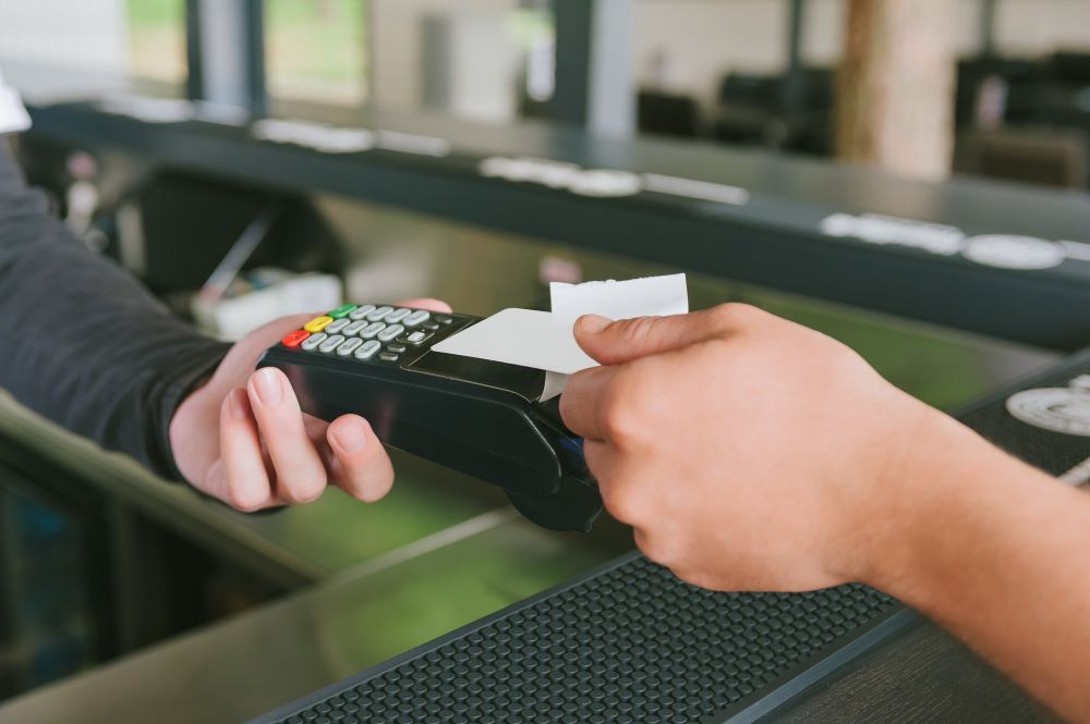 Pessoa pagando com cartão em um terminal POS em um balcão.
