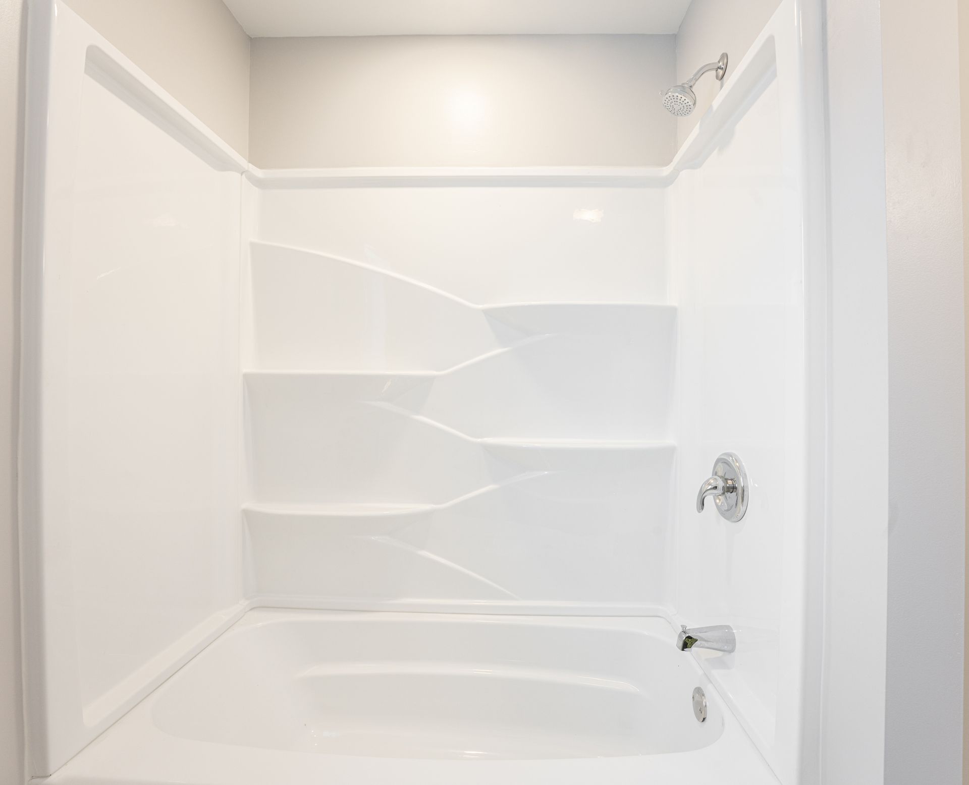 White bathtub and shower alcove with built-in shelves and chrome fixtures