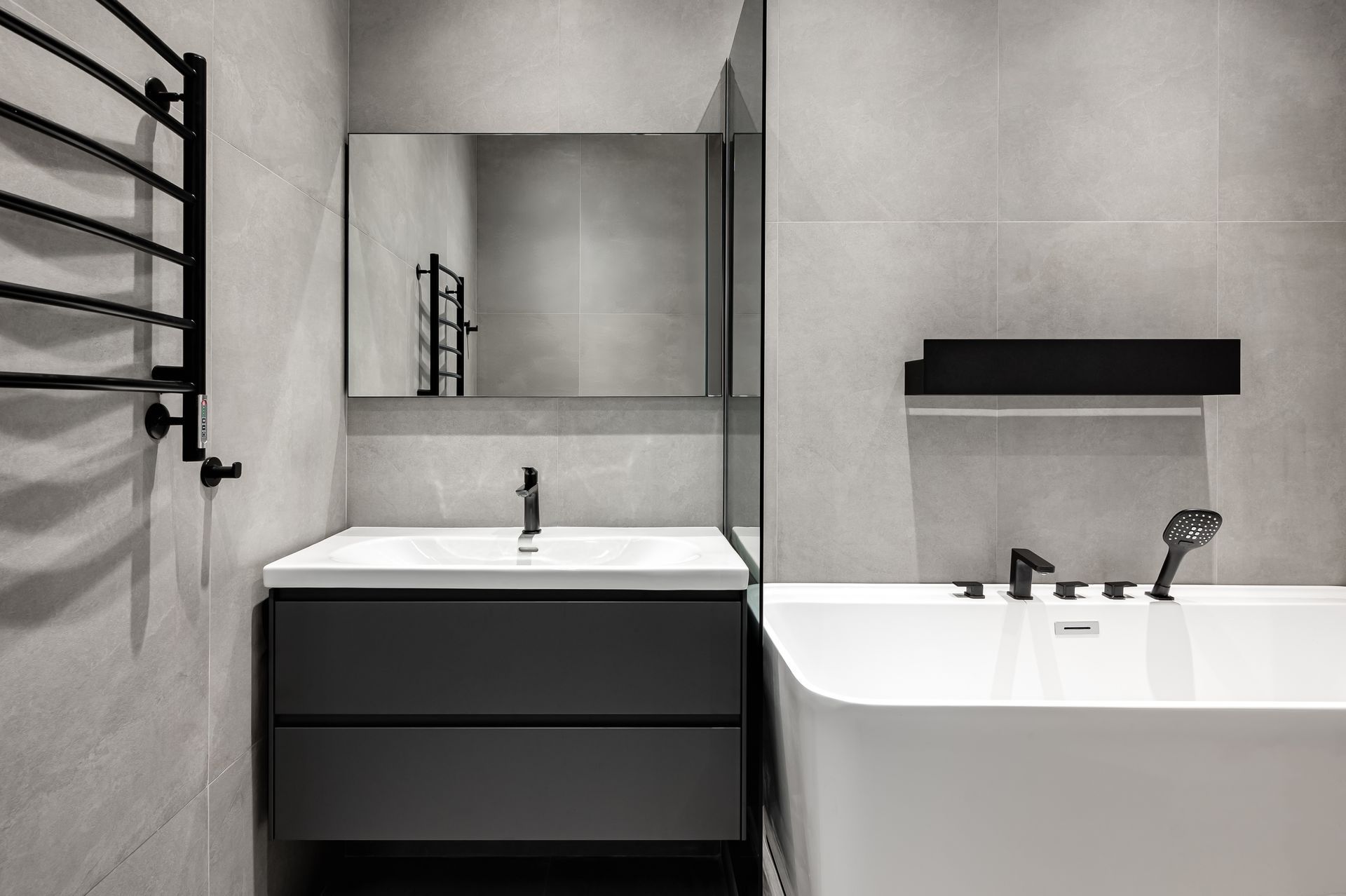 Modern gray bathroom with wall mirror, dark vanity, and white bathtub with black shelf