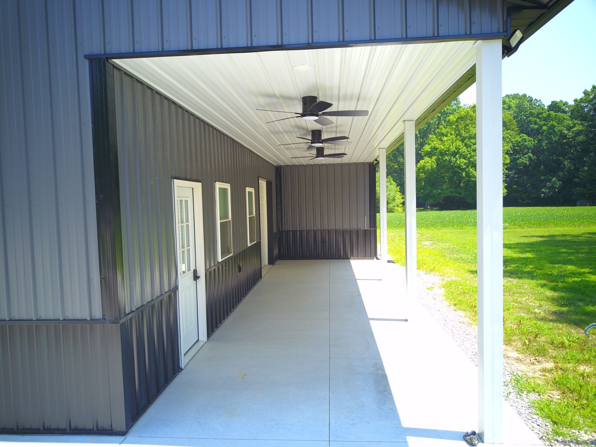 Long concrete porch with dark gray building and white columns. Three ceiling fans hang above.
