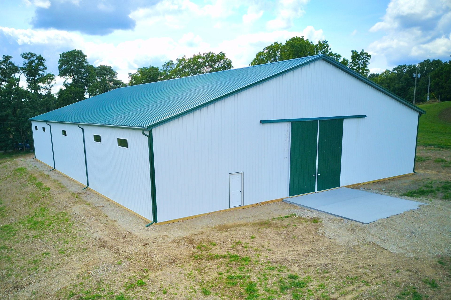 White and green barn with a green roof, set in a grassy field with trees in the background.