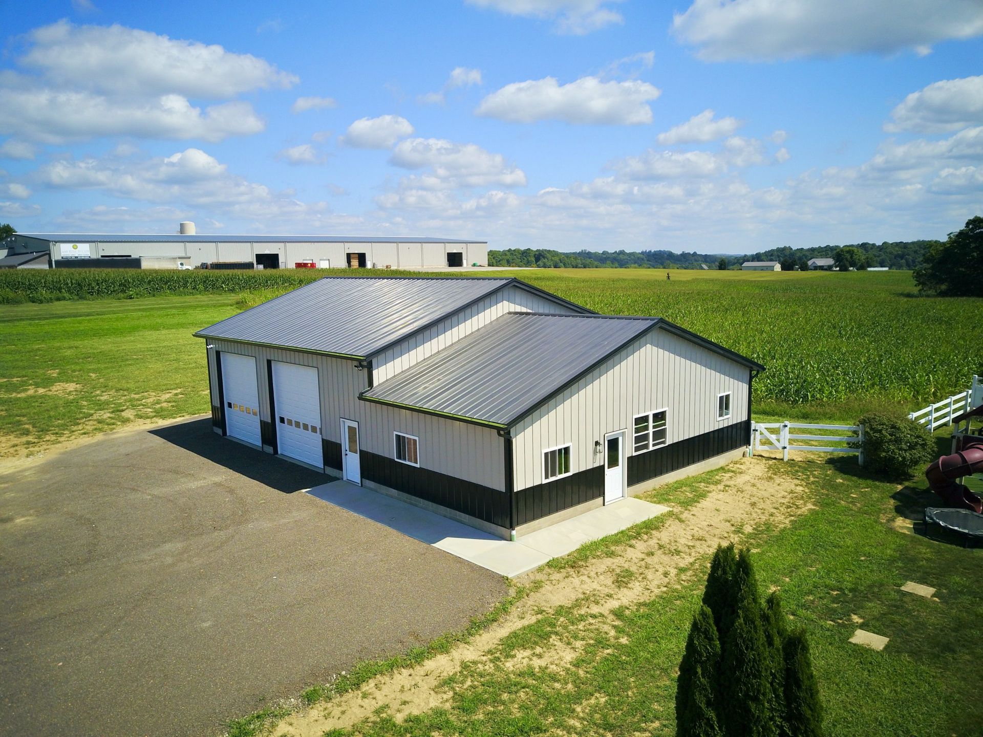 Aerial view of a gray and black metal building with three garage doors, set in a field under a blue sky.