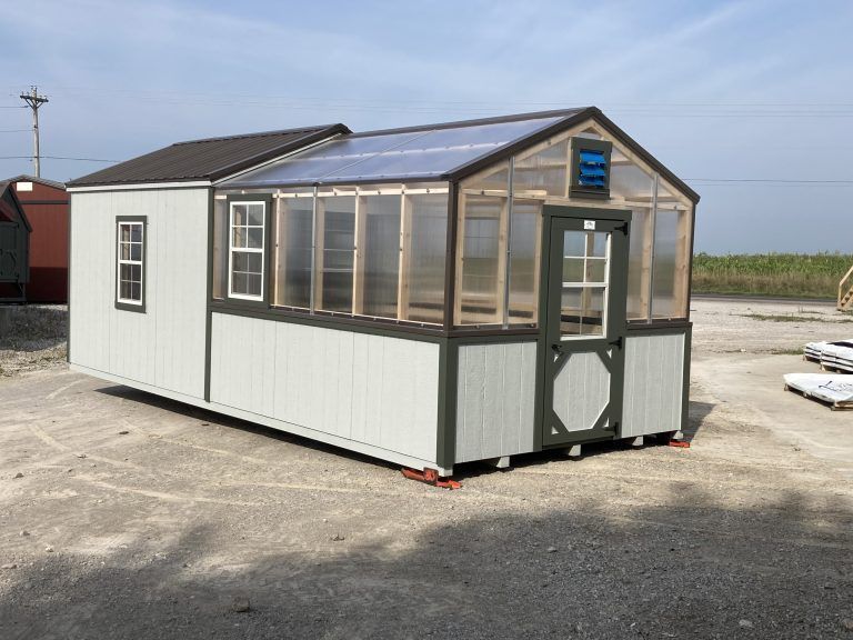 Light blue and green shed with a greenhouse section. The roof has clear panels and a small window. It's on a gravel surface.
