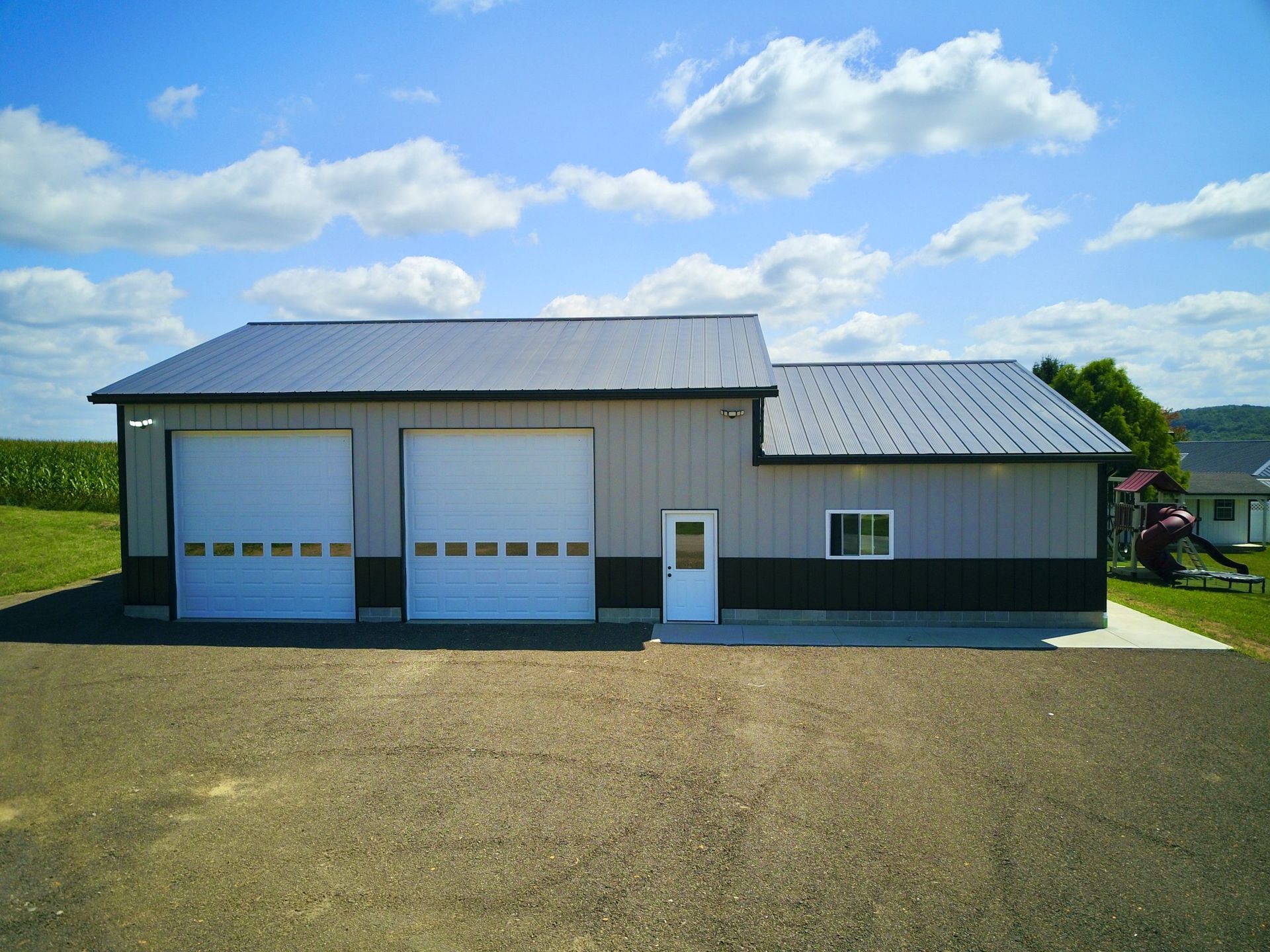 A large, gray metal building with two garage doors, a white door, and a small window set against a blue sky.