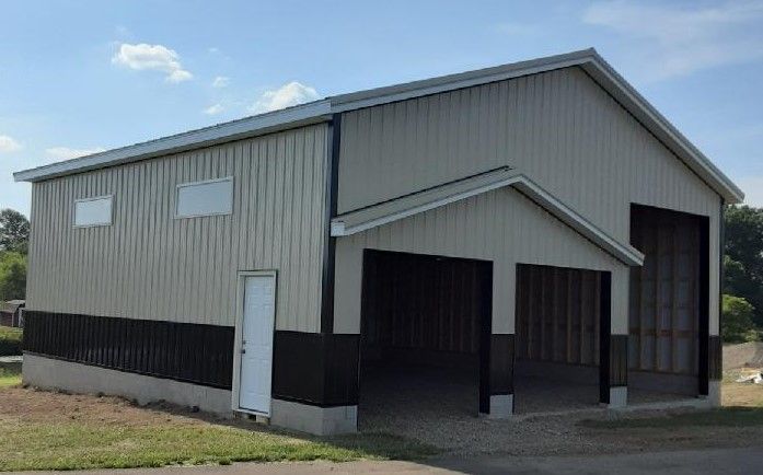Large metal building with tan and black siding, open bay, and white door on a sunny day.