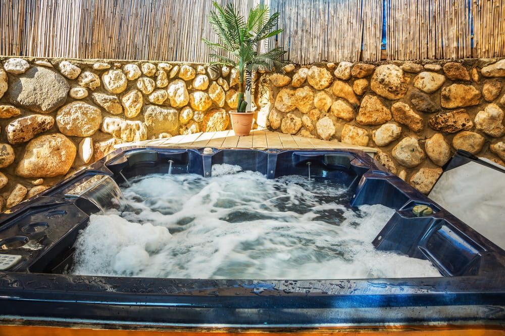 A Bubbling Hot Tub in a Stone-walled, Outdoor Setting — Intouch Pools & Spas in Forster, NSW